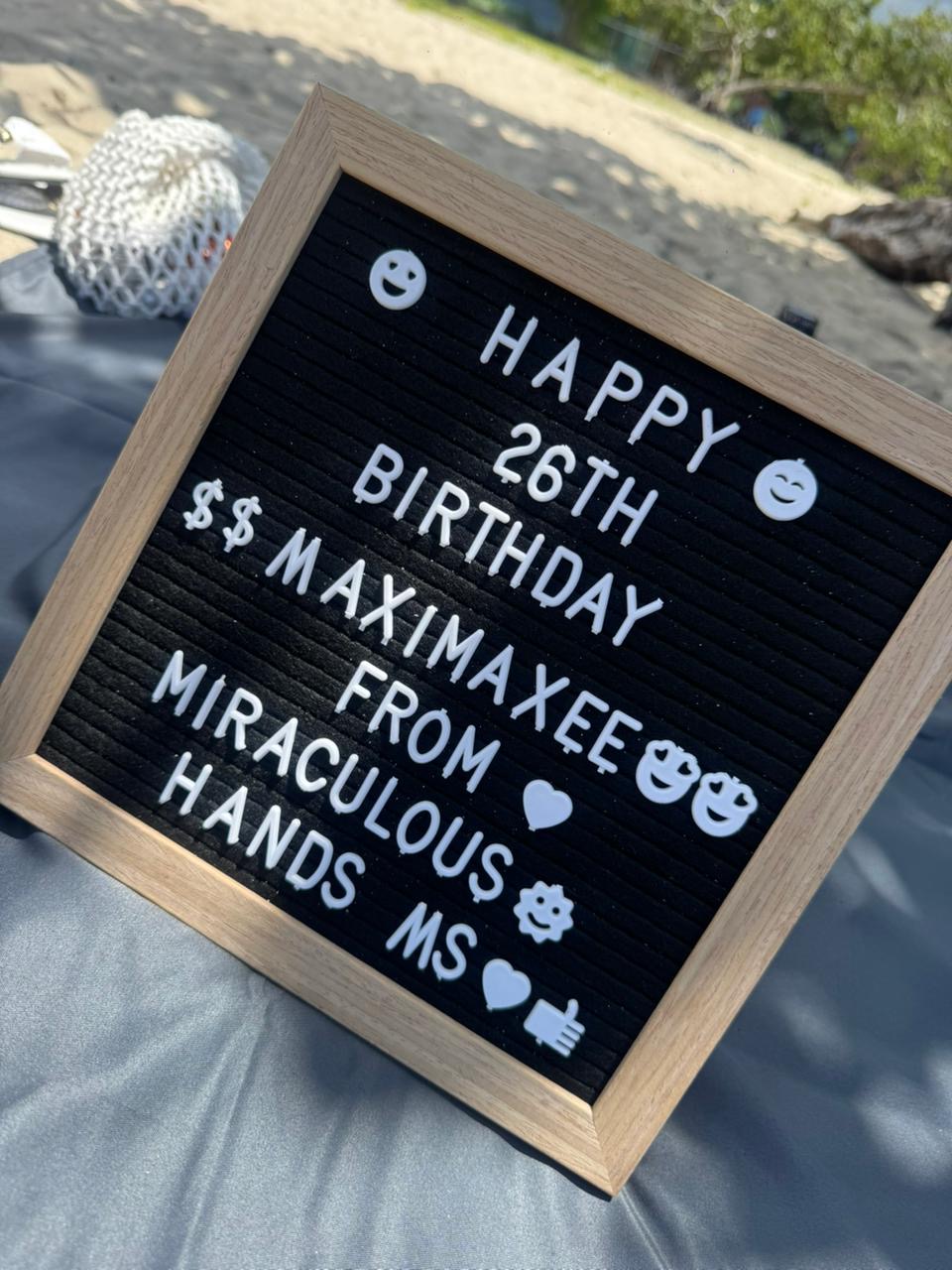 Black letter board reading Happy 26th Birthday from Miraculous Hands on a massage table at the beach